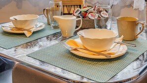 Une table à manger dressée avec des bols, des tasses et un pichet, agrémentée de rideaux en dentelle et offrant une vue sur des bâtiments en arrière-plan.