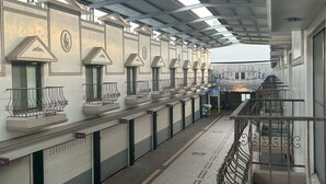 Un'area di attesa coperta con file di sedute, pavimento piastrellato e ringhiera in metallo.