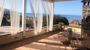 Un patio cubierto con una mesa y sillas, con vistas panorámicas al mar y edificios.