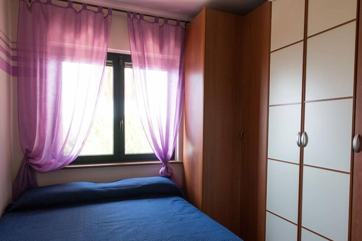 Un dormitorio con una cama, cortinas moradas, un ventanal y un armario.