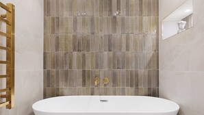 Un baño moderno con una bañera independiente, un toallero dorado y una pared de azulejos con un espejo.