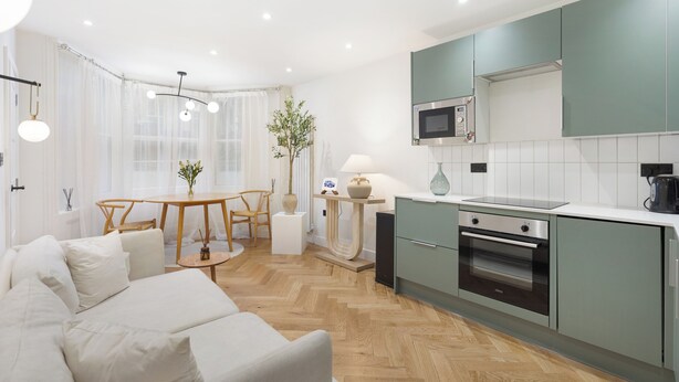 Una cocina moderna con gabinetes verdes, un horno integrado y un comedor con una mesa redonda y sillas.