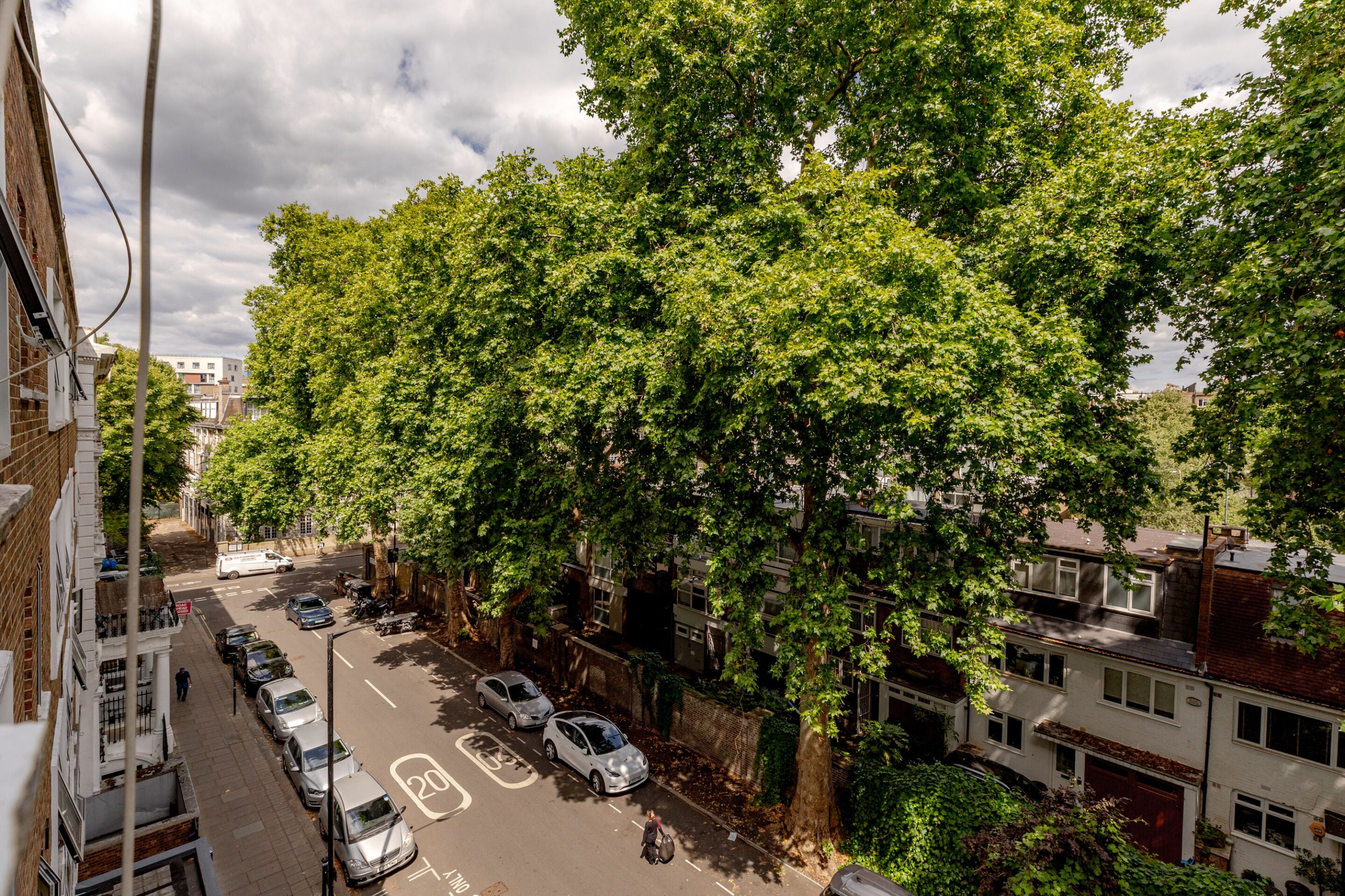 Eine Straße mit geparkten Autos und Bäumen, gesäumt von Gebäuden.