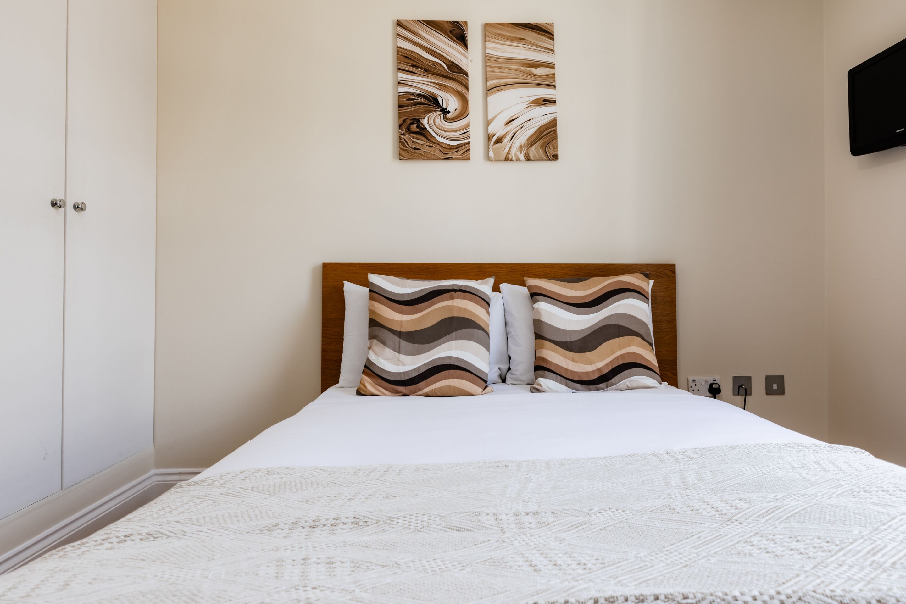 Una cama bien hecha con almohadas a rayas, un cabecero de madera y una manta blanca.