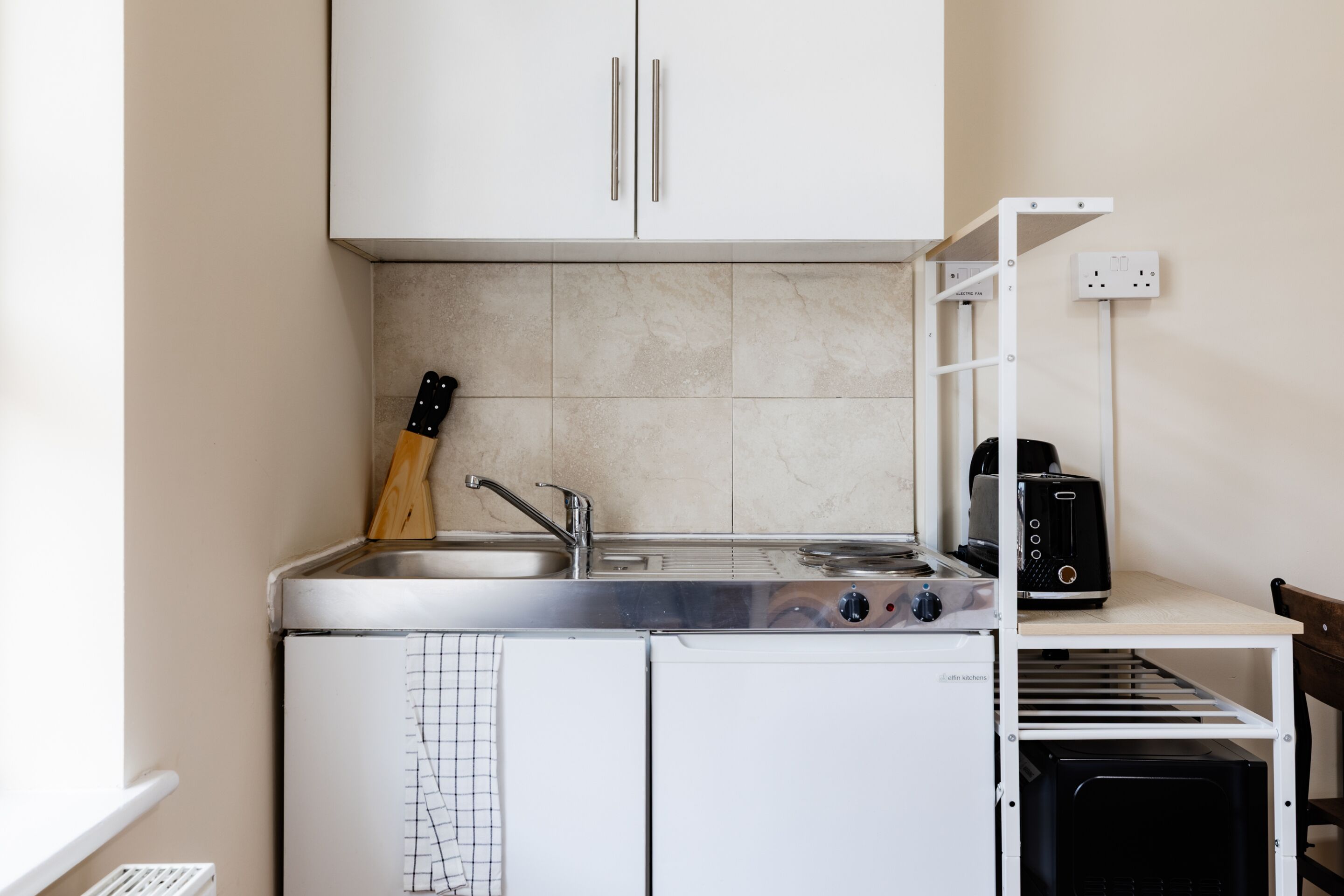 A compact kitchenette with a stove, sink, and a toaster.