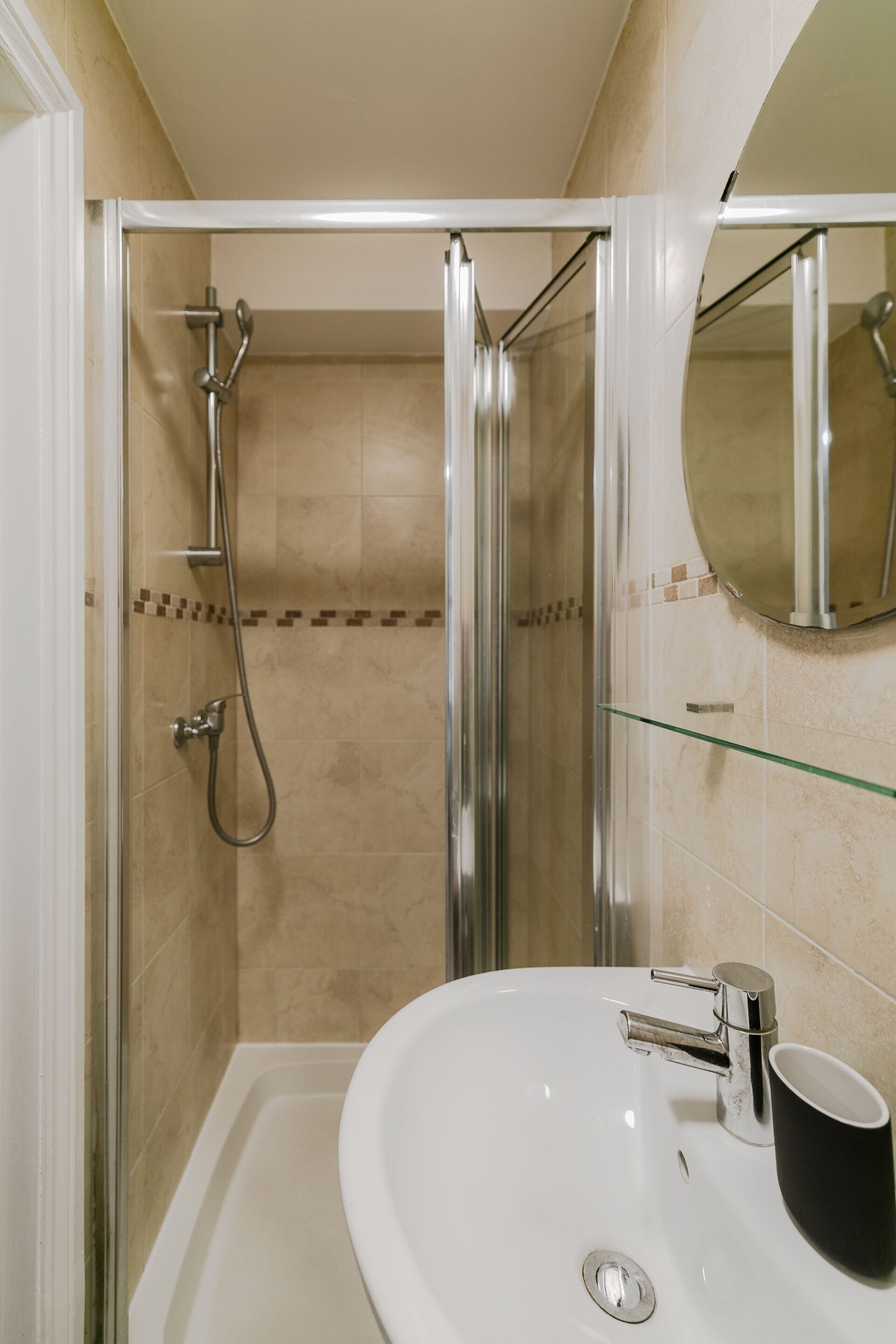 Un baño con cabina de ducha de vidrio, un lavamanos blanco con una taza negra y un espejo en la pared.