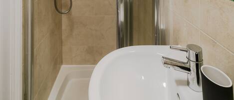 Un baño con cabina de ducha de vidrio, un lavamanos blanco con una taza negra y un espejo en la pared.