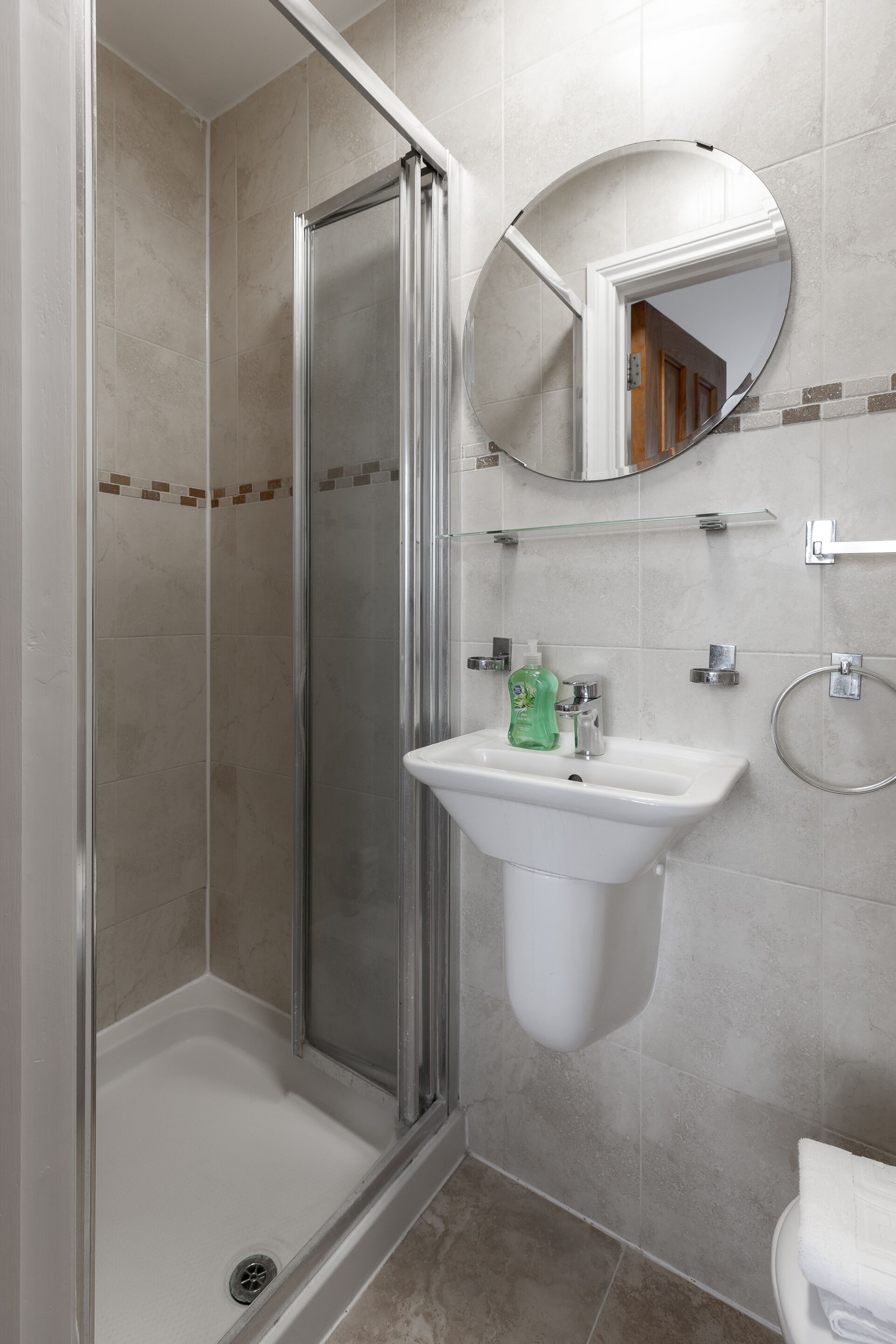 Une salle de bain avec une douche à parois de verre, un lavabo blanc avec un miroir au-dessus et des toilettes.