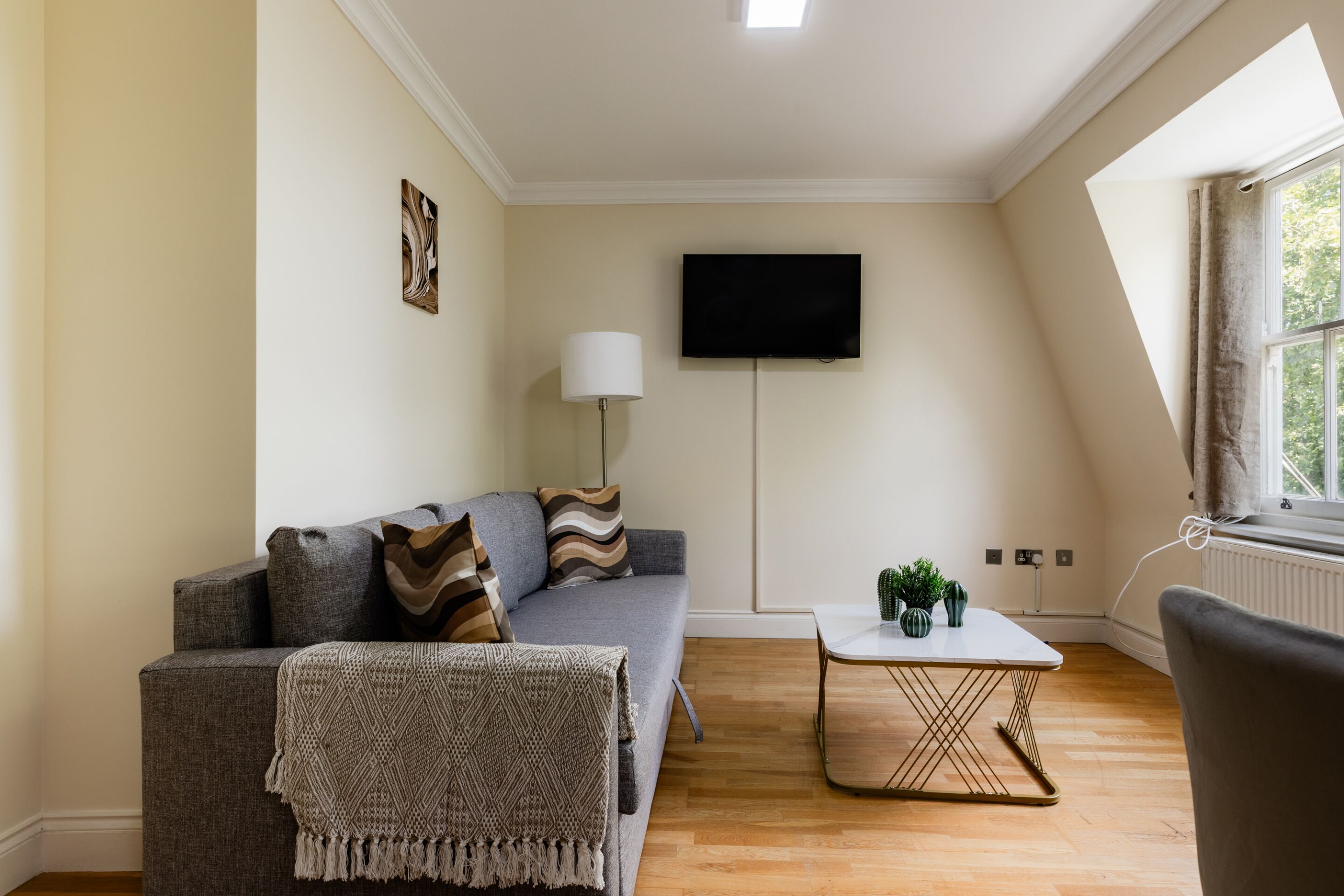 Un salon moderne avec un canapé gris, une table basse blanche et un téléviseur à écran plat fixé au mur.