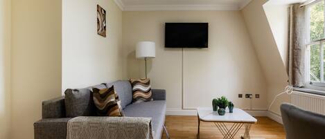 A modern living room with a grey sofa, a white coffee table, and a flat-screen TV mounted on the wall.