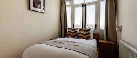 A bedroom with a bed, a window with curtains, a radiator, and a framed picture on the wall.