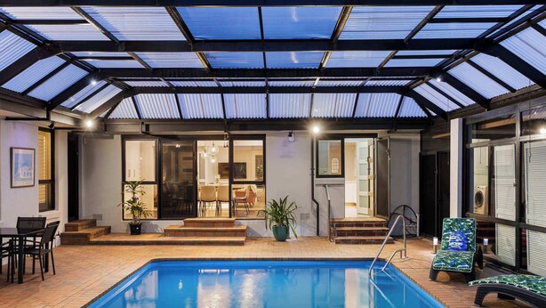 An indoor swimming pool with a glass ceiling, a dining area, and a staircase leading to a second level.