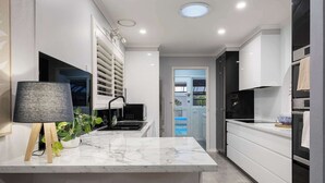 A modern kitchen with a marble countertop, two wooden stools, a black lamp, and a built-in oven.