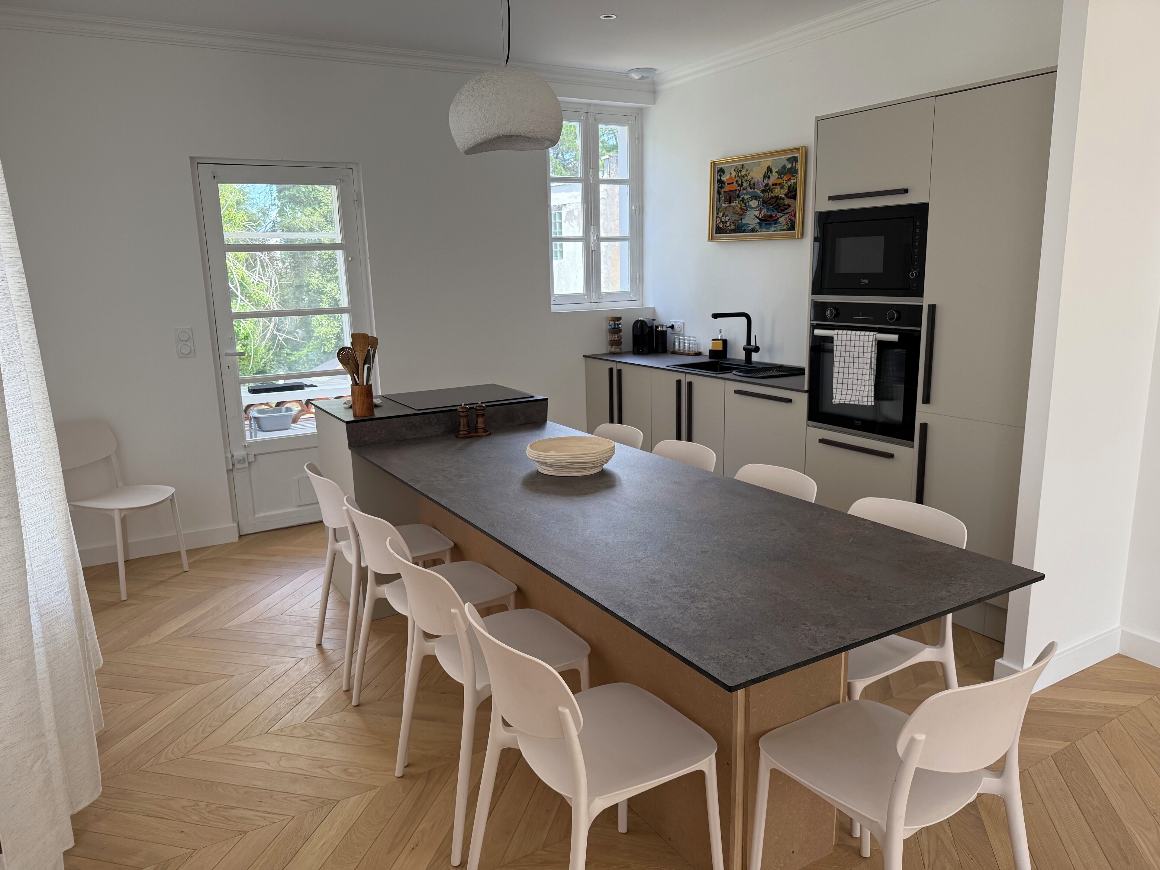 Eine moderne Küche mit einer Kochinsel, weißen Stühlen und einem großen Fenster.