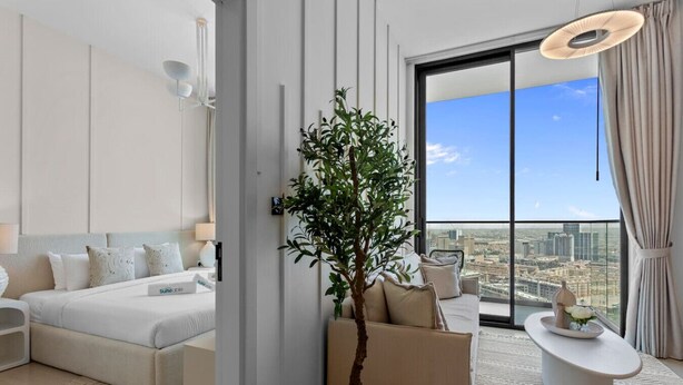 Ein modernes Hotelzimmer mit einem Bett, einer Sitzecke, einer Pflanze und Blick auf die Stadt.