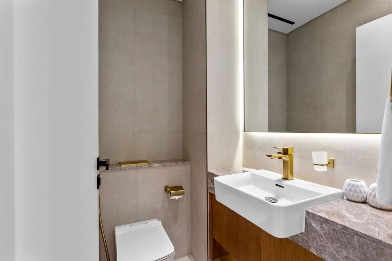 A modern bathroom with a white sink, gold fixtures, and a large mirror.