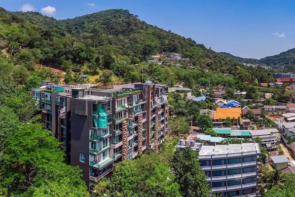 Un edificio de varios pisos con un diseño arquitectónico moderno, rodeado de exuberante vegetación y colinas al fondo.