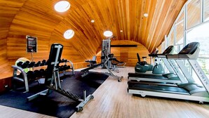 Een sportschool met houten wanden en plafond, loopbanden, gewichten en trainingsapparatuur.