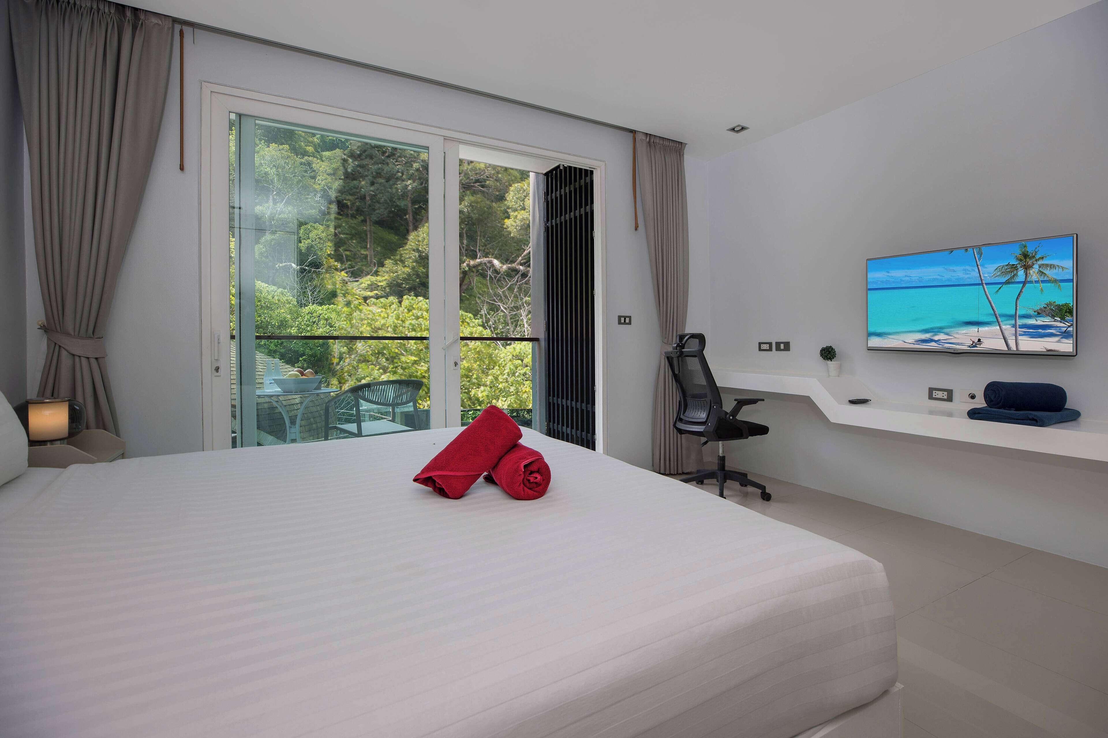 Ein Hotelzimmer mit einem großen Bett, einem an der Wand montierten Fernseher und einem Balkon mit Meerblick.