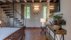 A bedroom with a wooden staircase, a bed, a nightstand, a lamp, a mirror, and a potted plant. - Corte Baruzzo Relais (Volta Mantovana)