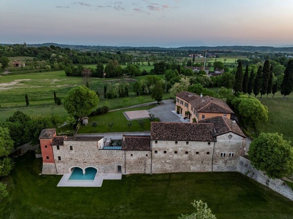 An aerial view of a historic building with a swimming pool, surrounded by lush greenery and fields. - Corte Baruzzo Relais (Volta Mantovana)