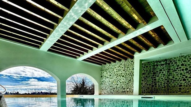 An indoor swimming pool with clear water, wooden beams on the ceiling, and a stone wall. - Corte Baruzzo Relais (Volta Mantovana)