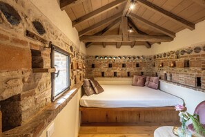 A rustic room with exposed brick walls, a wooden ceiling, and a bed with a wooden platform.