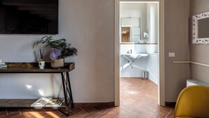 A modern interior with a wooden desk, books, and decorative items. A doorway leads to a bathroom with a sink and mirror. - Corte Baruzzo Relais (Volta Mantovana)