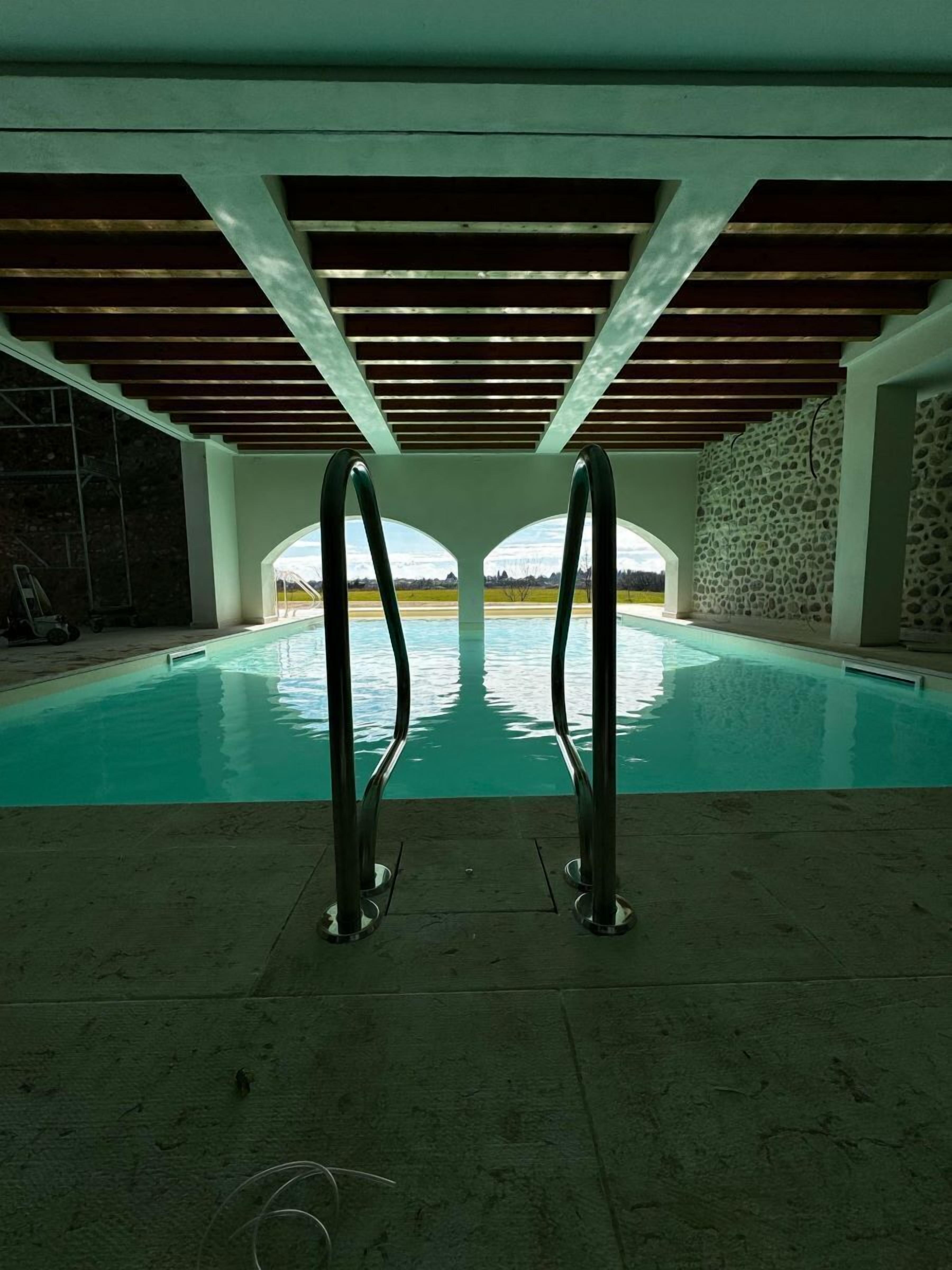 Ein Hallenbad mit zwei Sprungbrettern, einer Steinwand und Blick auf die Landschaft.