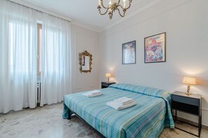 Quarto de hotel com cama, duas mesas de cabeceira, um lustre, um espelho e duas obras de arte emolduradas na parede.