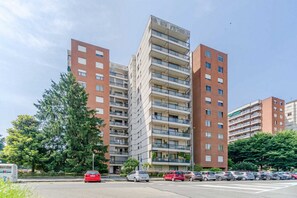 Um edifício residencial com vários andares, varandas, um estacionamento e céu claro.