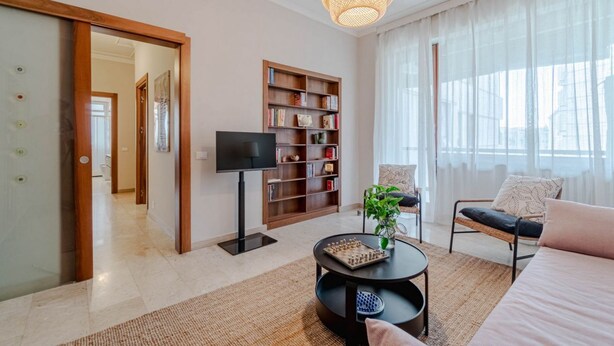 A modern living room with a flat-screen TV, a bookshelf, a sofa, a coffee table, and a large window with sheer curtains. - GuestHost - Cozy apartment of about 80 sqm, able to accommodate up to 5 people, located on the fourth floor of a building with a lift.The property is located in a residential neighborhood of Turin, in an area full of all comforts and well connected to th (Turin)