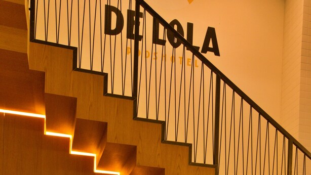 A staircase with wooden steps and a black handrail, leading to a room with a bed and pillows.