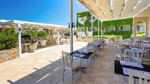An outdoor patio area with tables and chairs, covered by a canopy, and surrounded by greenery. - Dias by Azul Collection (Rethymno)