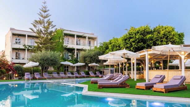 A swimming pool with lounge chairs and umbrellas, surrounded by greenery and a building with balconies. - Dias by Azul Collection (Rethymno)