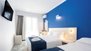 A hotel room with two beds, a TV, a bedside table, a nightstand, and a window with curtains. - Dias by Azul Collection (Rethymno)