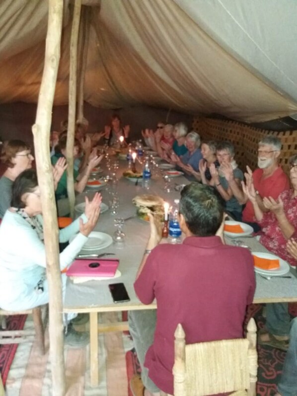 A group of people seated around a table in a tent-like structure, clapping.