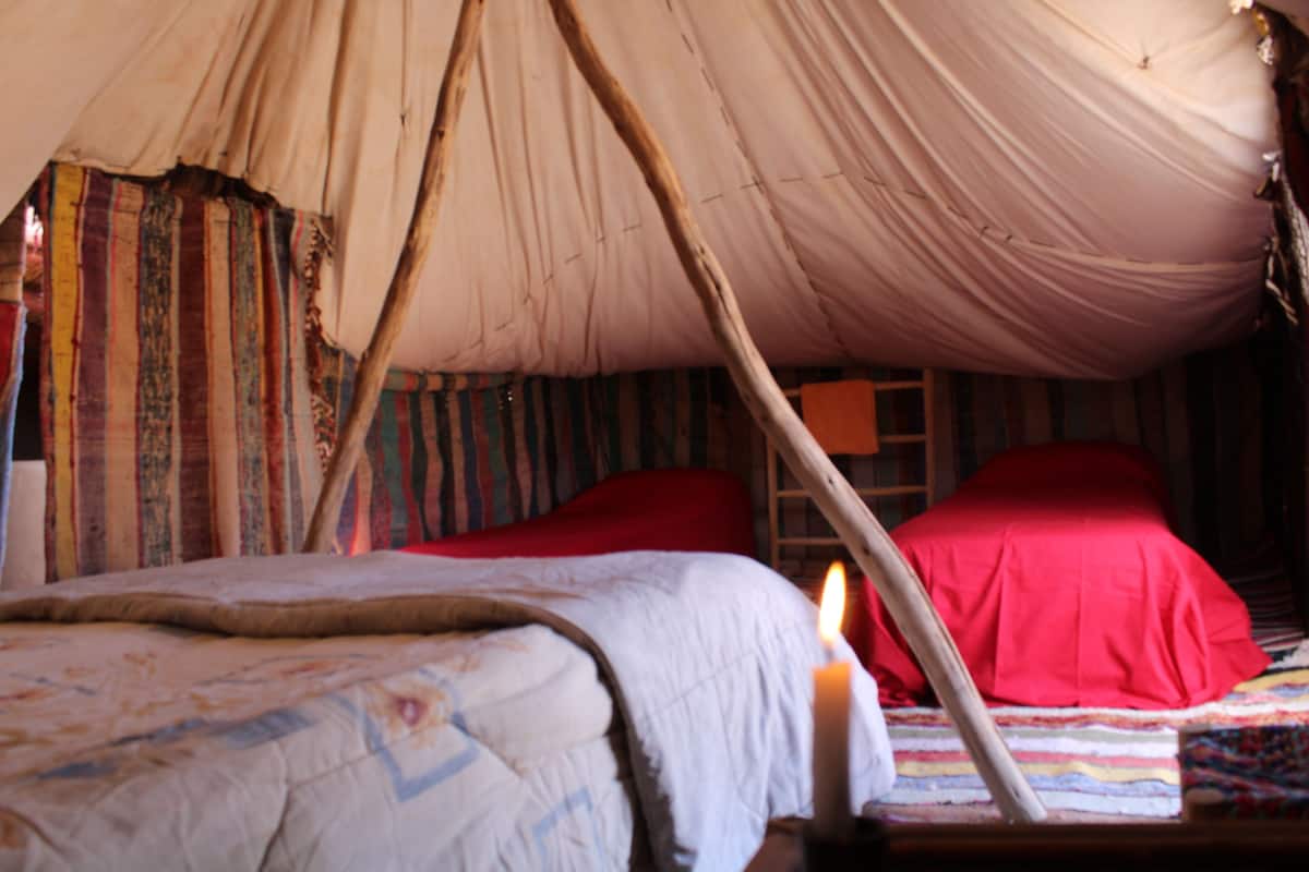 A tent with a bed inside, featuring a red blanket and a lit candle.