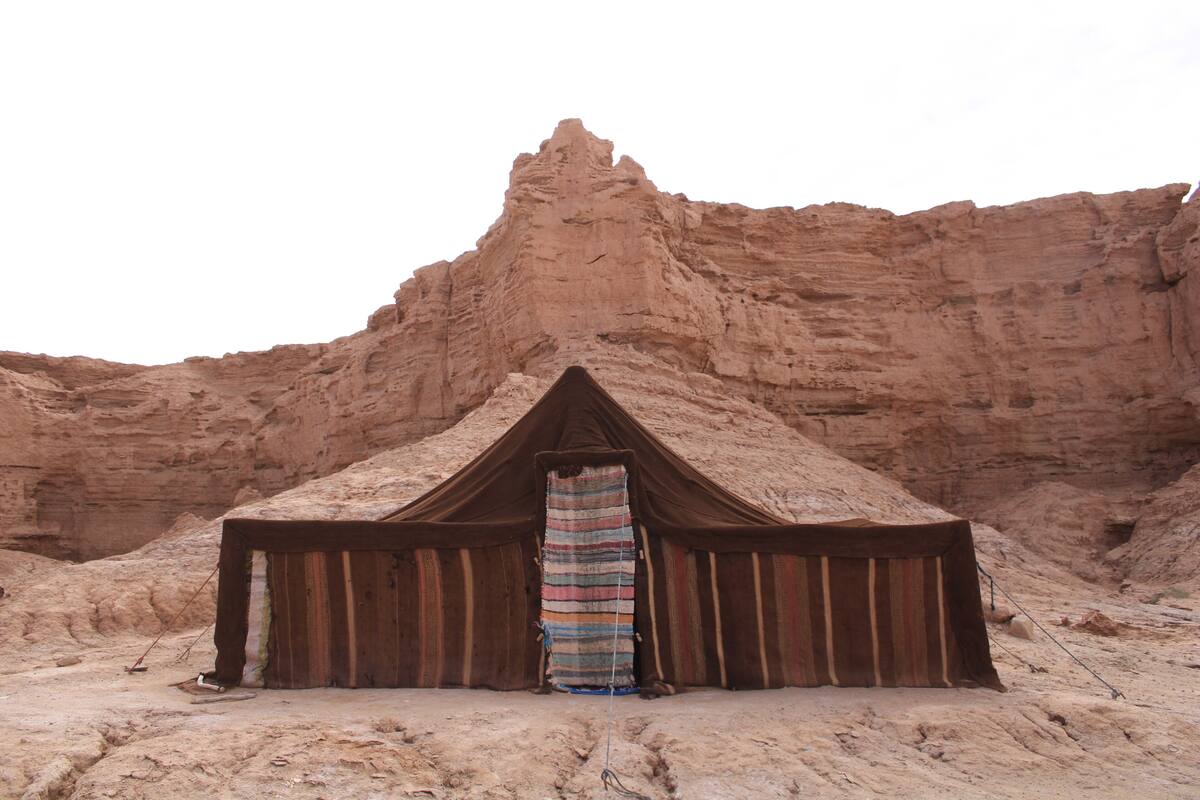 A tent-like structure with a striped fabric entrance, set against a rocky desert backdrop.