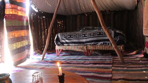 Una habitación acogedora con una cama, una mesa con una vela y un tapete rayado de colores.
