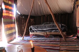 Una habitación acogedora con una cama, una mesa con una vela y un tapete rayado de colores.