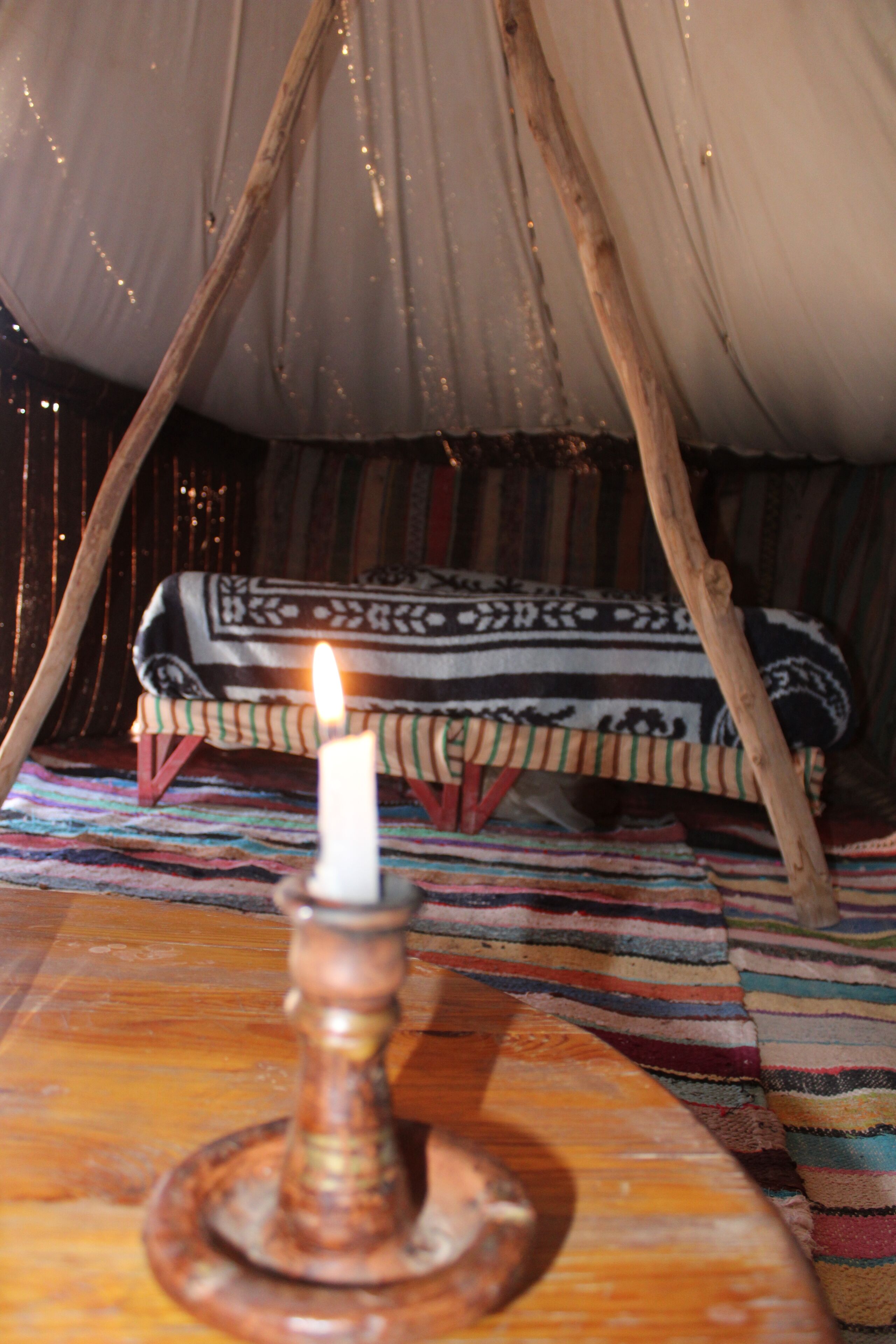 A cozy interior with a wooden table, a lit candle, and a patterned blanket on a striped rug.