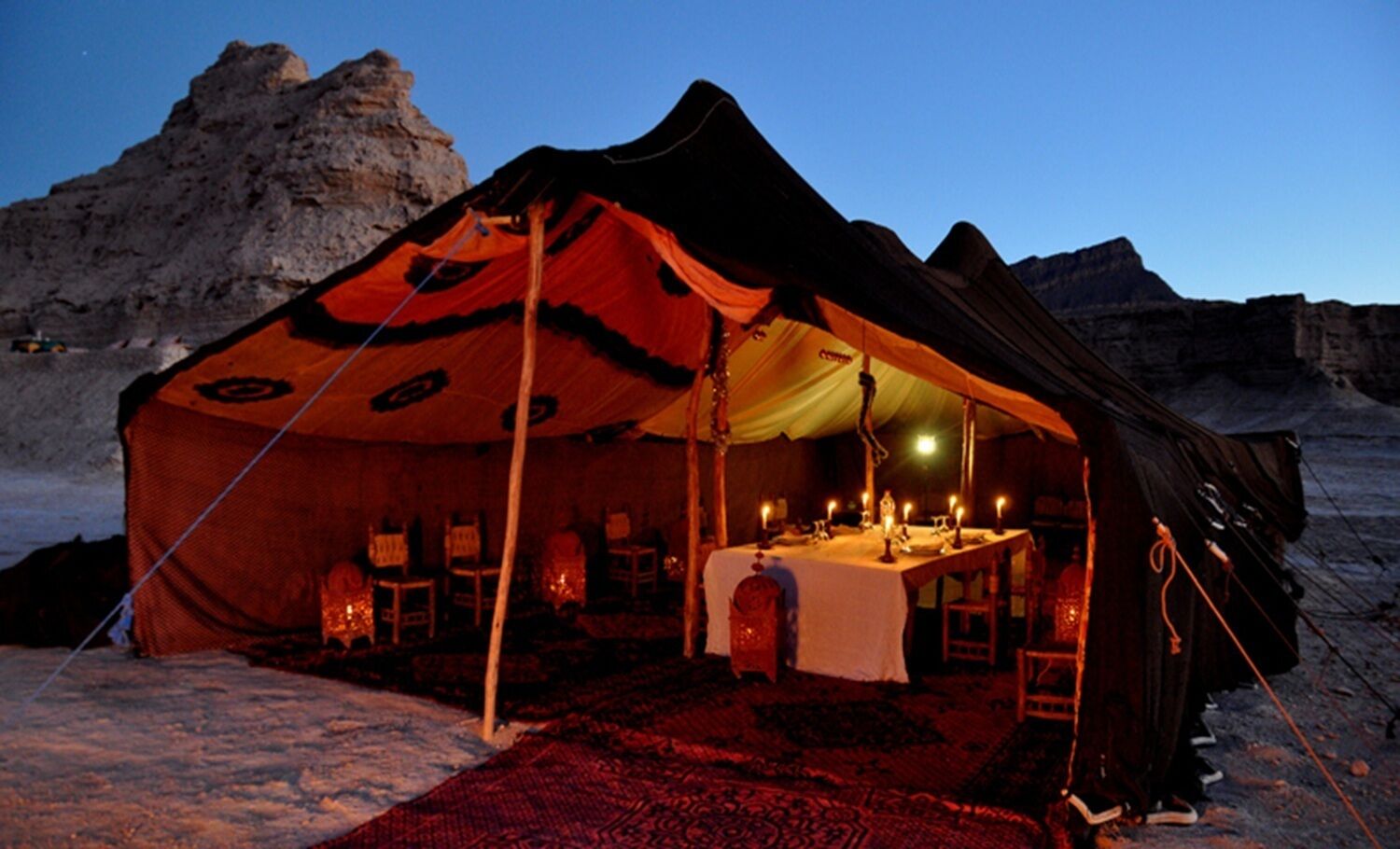 A tent with a dining table set up inside, surrounded by chairs, in a snowy outdoor setting.