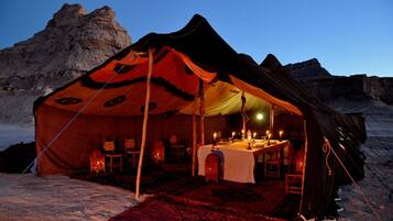 A tent with a dining table set up inside, surrounded by chairs, in a snowy outdoor setting.