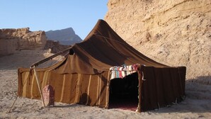 Una tienda de campaña en el desierto con una única entrada, frente a un paisaje rocoso.