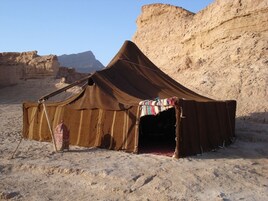 Una tienda de campaña en el desierto con una única entrada, frente a un paisaje rocoso.