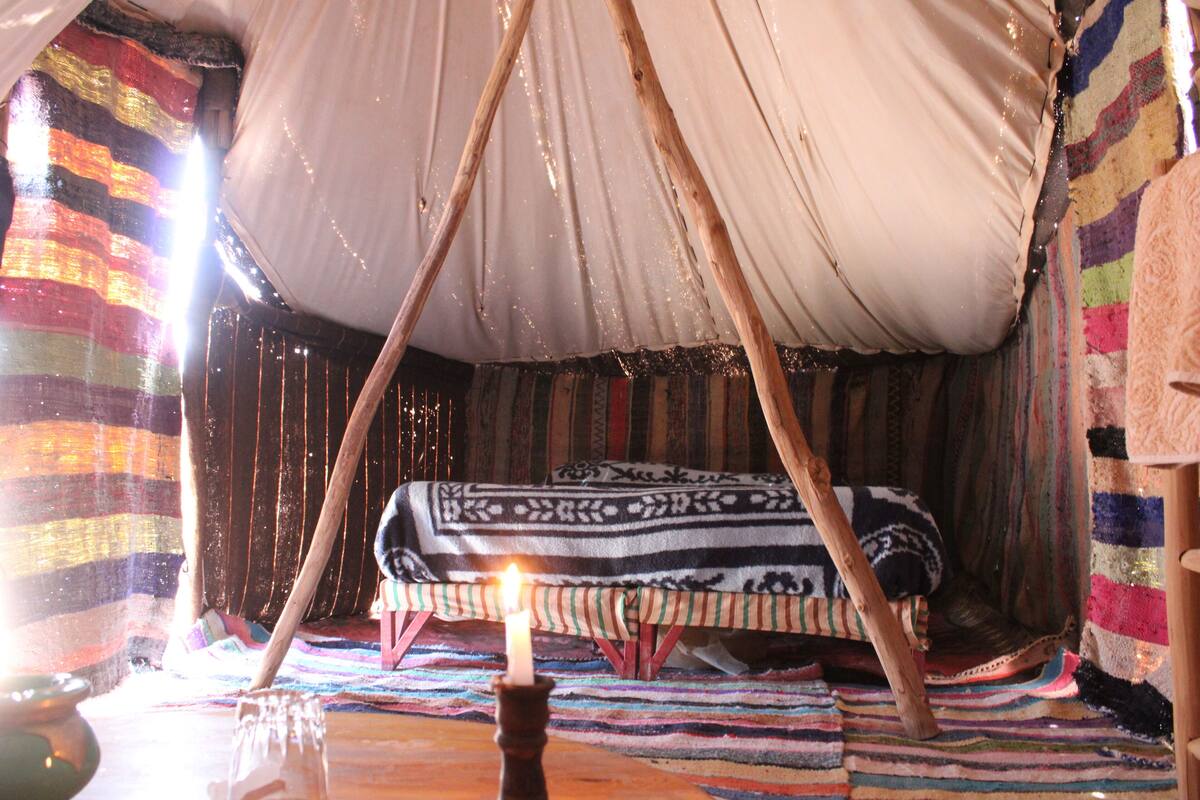 A cozy, tent-like room with a bed, a candle, and a colorful striped wall.