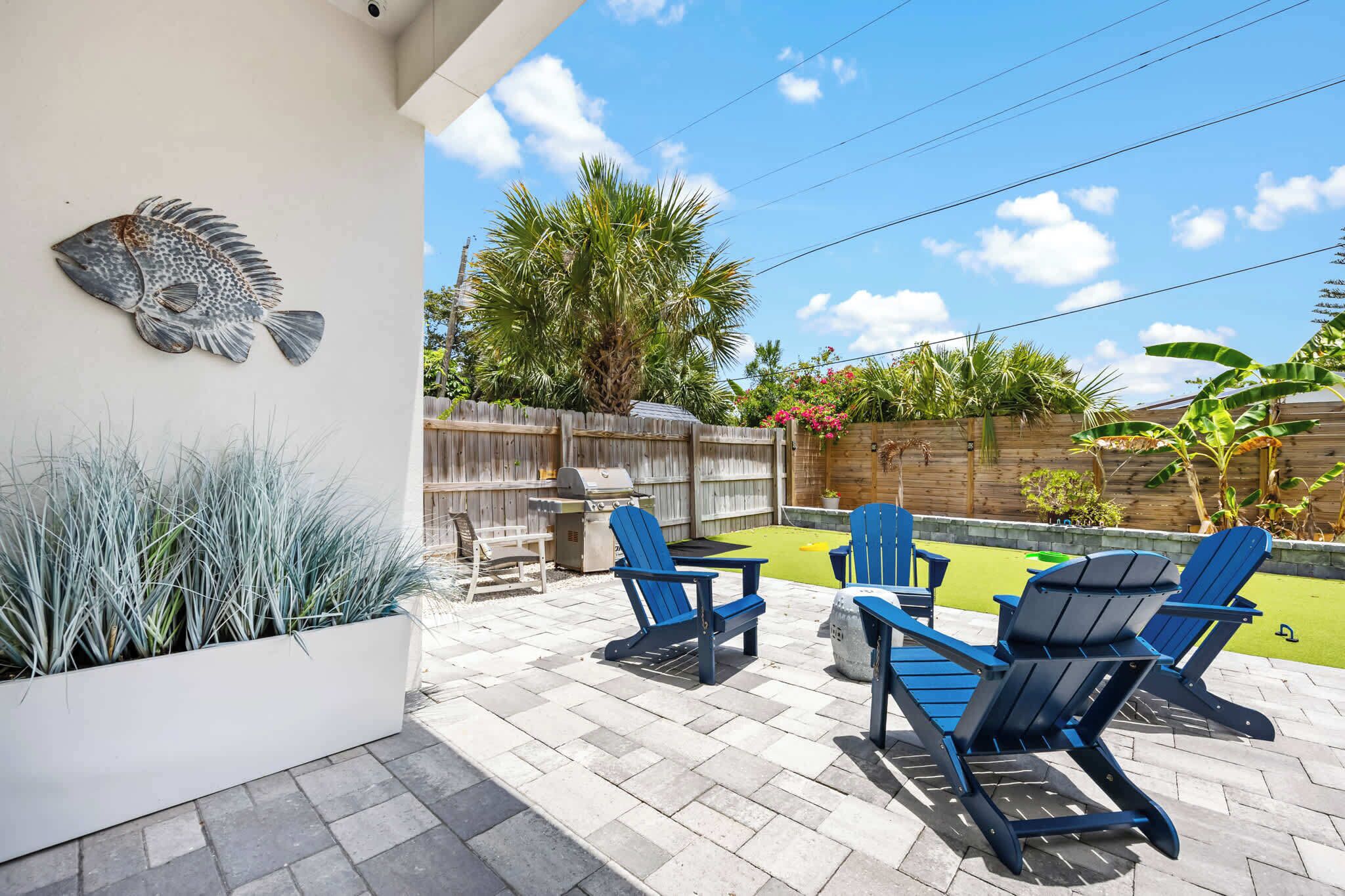 Un patio con sillas Adirondack azules, una parrilla para barbacoa y una decoración con motivos de peces.