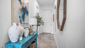 Un couloir avec une console bleue, des vases blancs, une lampe et un miroir.