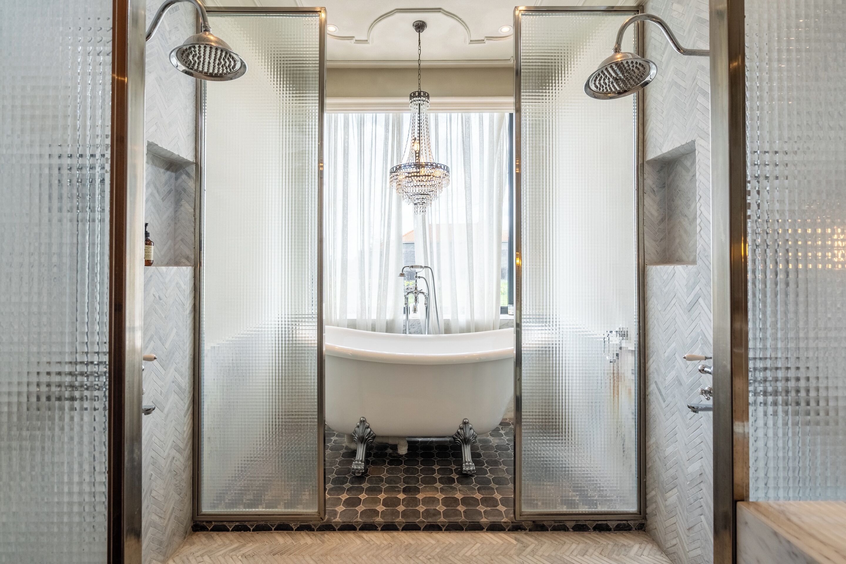 A luxurious bathroom with a freestanding bathtub, a modern shower, and a chandelier.